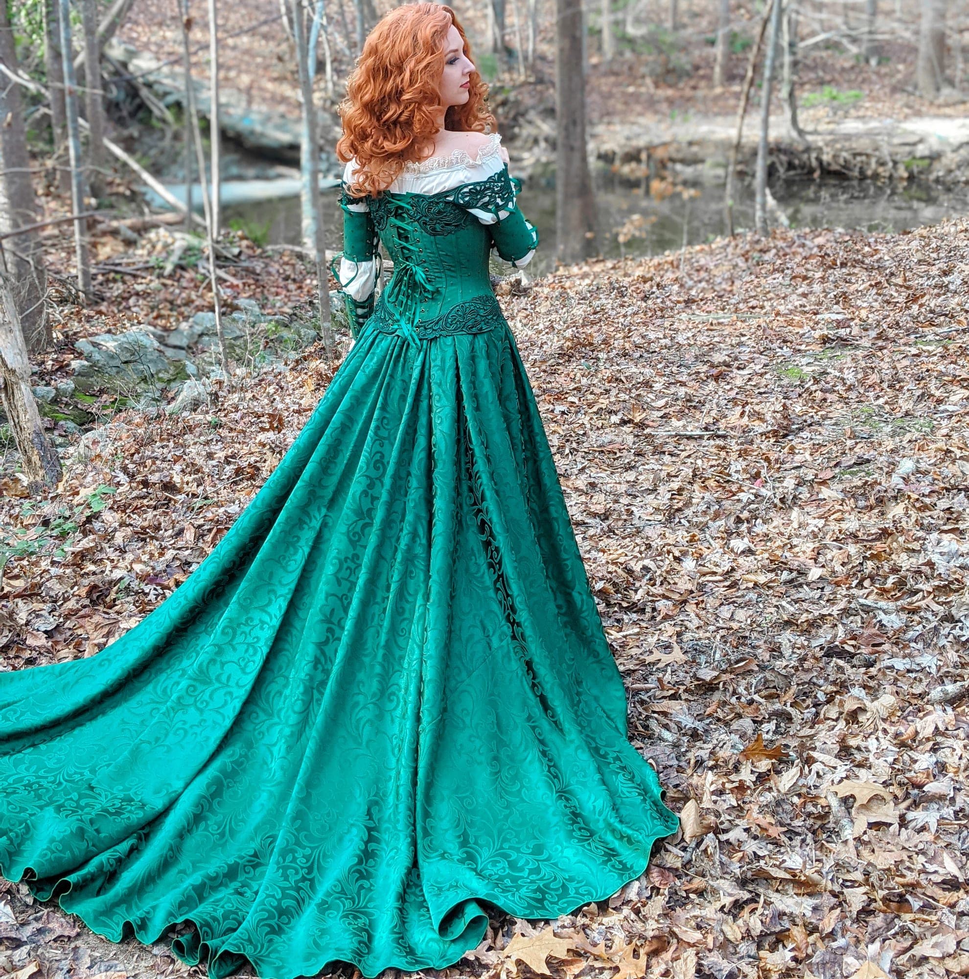 Emerald green medieval gown with a long train, photographed from behind in the woods