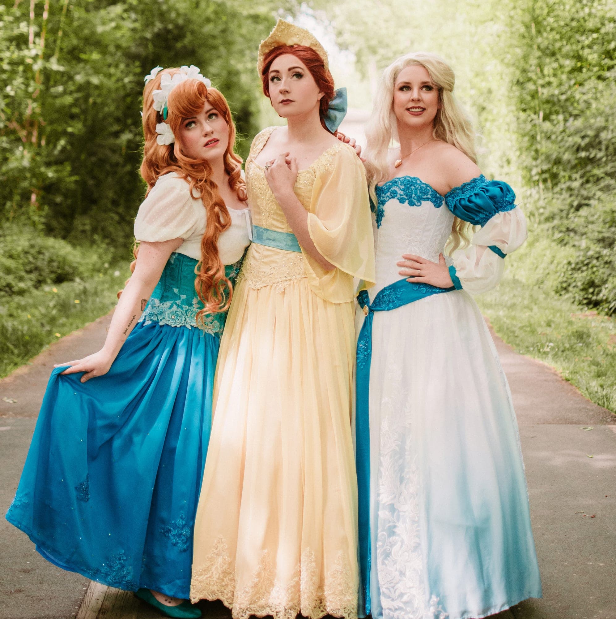 Three women in fairytale princess gowns posing on a garden path