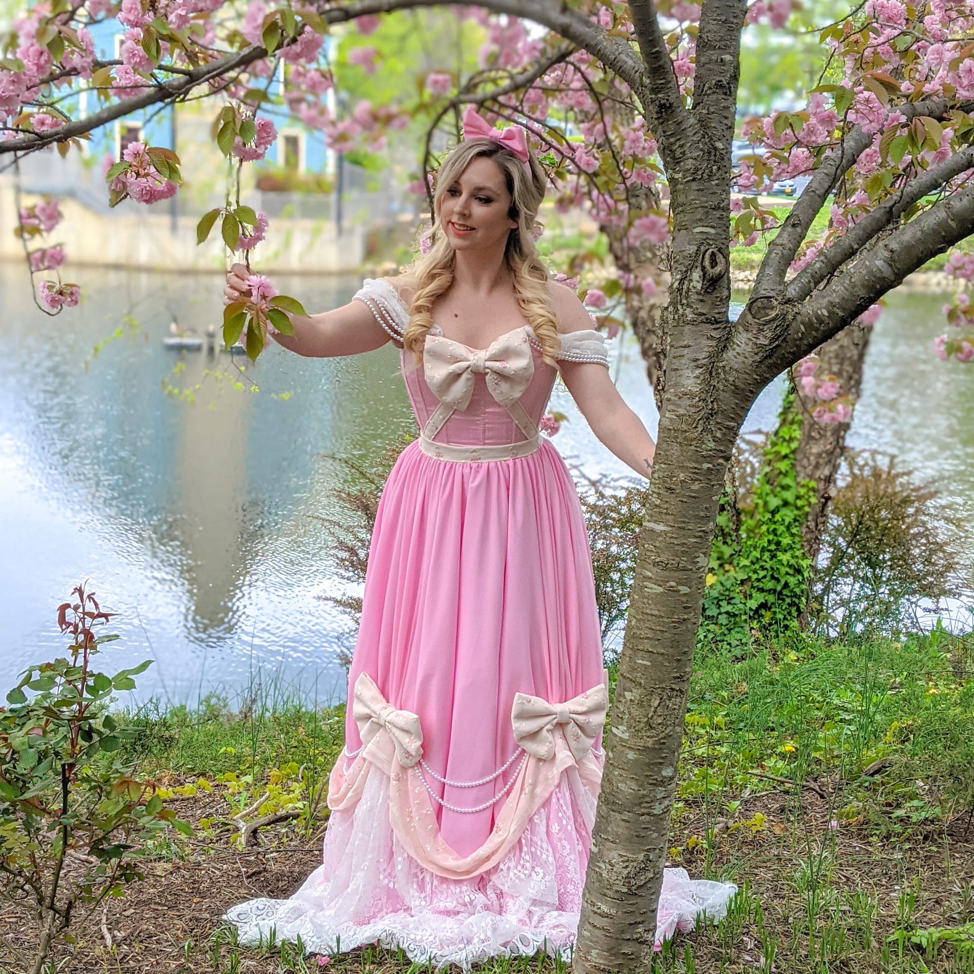 Pink off-the-shoulder gown with bows and a lace hem beneath cherry blossoms