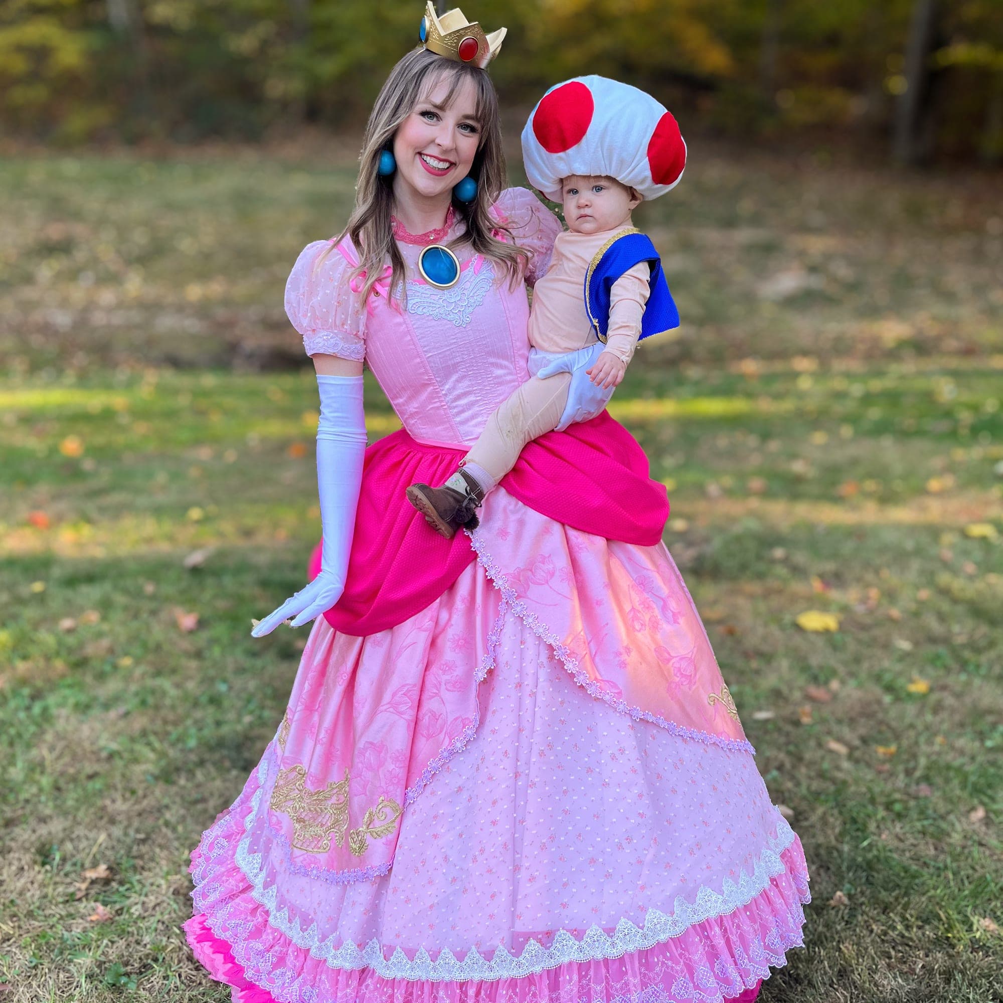 Woman in a handmade Princess Peach ball gown holding a baby in a Toad costume
