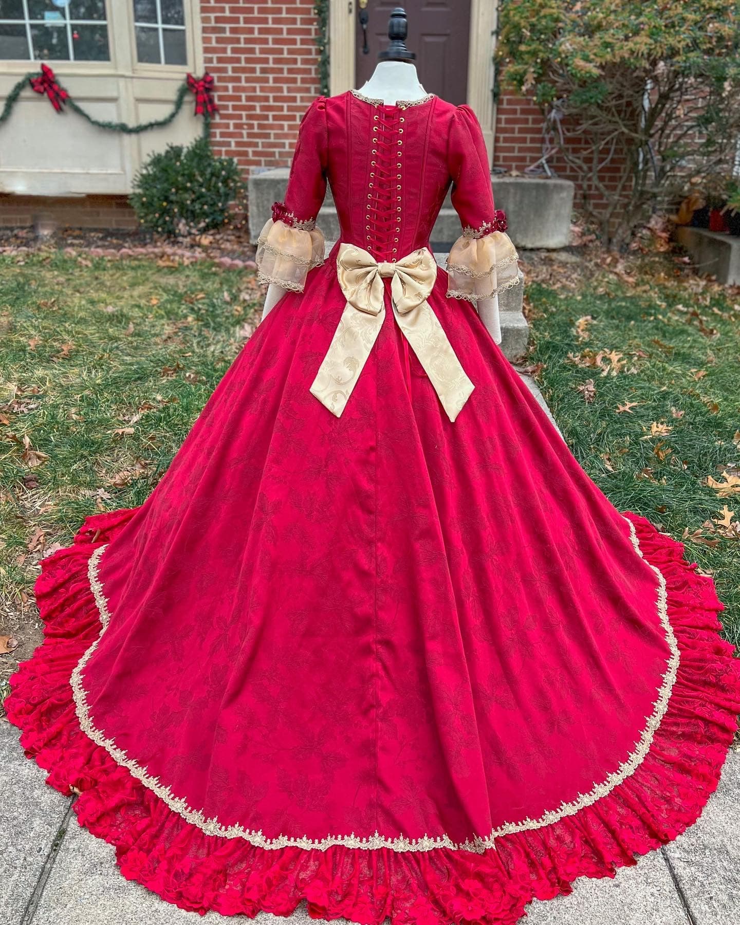 Deep red Victorian ball gown with a cream bow and ruffled train on a dress form